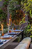 TANYA SOUTHWORTH GARDEN, LONDON, DESIGNER ANOUSHKA FEILER: SMALL GARDEN - TABLE, BENCHES, CANDLES, RENDERED WALL WITH CIRCLE THROUGH IT, LIGHTING, EVENING, NIGHT, FORMAL