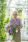 CLAUS DALBY GARDEN, DENMARK: CLAUS DALBY IN HIS GREENHOUSE HOLDING A BOUQUET OF FLOWERS FROM THE GARDEN