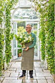 CLAUS DALBY GARDEN, DENMARK: CLAUS DALBY IN HIS GREENHOUSE HOLDING  A BOUQUET OF WHITE FLOWERS FROM THE GARDEN