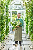 CLAUS DALBY GARDEN, DENMARK: CLAUS DALBY IN HIS GREENHOUSE HOLDING  A BOUQUET OF WHITE FLOWERS FROM THE GARDEN
