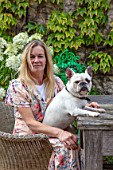 PYTTS HOUSE, OXFORDSHIRE: OWNER ANNA DE KEYSER WITH HER DOG MABLE ON THE TERRACE OUTSIDE THE HOUSE, PATIO, SUMMER. PARASOL