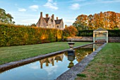 RADCOT HOUSE, OXFORDSHIRE: THE HOUSE SEEN FROM THE LONG POND. BEECH HEDGES, HEDGING, POOL, CANAL, GAZEBO, SEAT, SEATING, AUTUMN, REFLECTIONS, REFLECTED