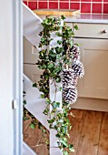 THE CONIFERS, OXFORDSHIRE: CHRISTMAS - KITCHEN DINING ROOM - STAIRCASE WITH IVY AND WHITE SPRAYED PINE CONES, DECORATIONS, NATURAL