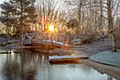THE OLD RECTORY, QUINTON, NORTHAMPTONSHIRE: DESIGNER ANOUSHKA FEILER: LAKE, POOL, POND, WATER, WOODEN BRIDGE, FROST, WINTER, FROSTY GARDEN, ENGLISH, COUNTRY, DAWN, SUNRISE