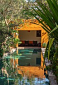TAROUDANT, MOROCCO: DESIGNERS ARNAUD MAURIERES AND ERIC OSSART: DAR AL HOSSOUN - EXOTIC PLANTING BESIDE POOL, WATER, CANAL, LOGGIA, ORANGE, CUSHIONS, SEATING