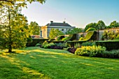WINSON MANOR, GLOUCESTERSHIRE: LAWN, BORDER BESIDE WALL, MANOR HOUSE BEHIND, ENGLISH, COUNTRY, GARDENS, SUMMER