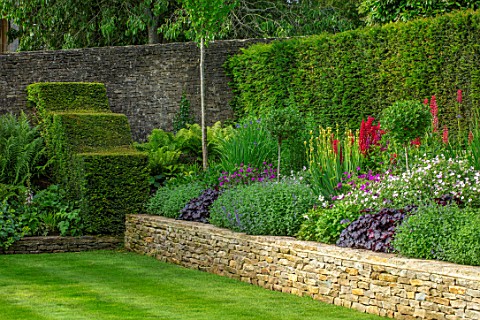 WINSON_MANOR_GLOUCESTERSHIRE_BORDERS_IN_RAISED_STONE_WALL_BED_LUPINS_HEUCHERAS_SUMMER_YEW_HEDGING_HE