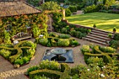 MANOR FARM, CHESHIRE: VIEW ONTO FORMAL HERB GARDEN - STEPS, GRAVEL, WATER FEATURE, BOX HEDGES, HEDGING, AMSONIA SALICIFOLIA, LAWN, WOODEN BENCH