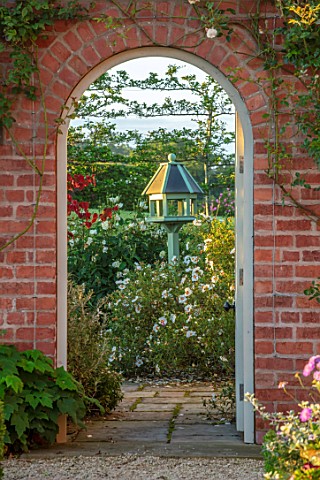 MANOR_FARM_CHESHIRE_VIEW_THROUGH_GATE_BRICK_ARCH_TO_BIRDFEEDER_AND_TERRACE_WITH_CISTUS_CYPRIUS_FOCAL
