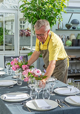 CLAUS_DALBY_GARDEN_DENMARK_CLAUS_PUTTING_VASES_OF_ROSES_ON_OUTDOOR_TABLE