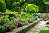 WINSON MANOR, GLOUCESTERSHIRE: PATIO, TERRACE, RAISED BED, GERANIUMS, ROSES, WISTERIA, HEUCHERAS, CLIPPED TOPIARY YEW SHAPES ON LAWN, SUMMER