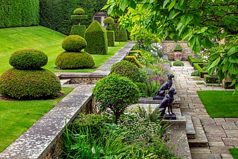 WINSON_MANOR_GLOUCESTERSHIRE_LAWN_RAISED_BED_YEW_TOPIARY_ON_LAWN_CATALPA_STATUES_WALLS_SUMMER_BORDER