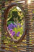 THE NEWT IN SOMERSET: THE BLUE GARDEN, JULY, PHLOX BLUE PARADISE SEEN THROUGH CIRCULAR WINDOW IN WICKER FENCE, FENCING, BOUNDARY, BOUNDARIES