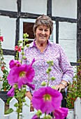 THATCH COTTAGE, WORCESTERSHIRE: OWNER MARY COX SURROUNDED BY TALL HOLLYHOCKS