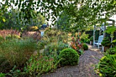 MITTON MANOR, SHROPSHIRE: THE ROUNDHOUSE GARDEN - WOODEN PERGOLA, SEAT, BENCH, PATH, BOX TOPIARY IN WOODEN VERSAILLES CONTAINERS, CANNAS, BOX BALLS, STIPA GIGANTEA, FORMAL, ENGLISH