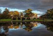 THORP PERROW ARBORETUM, YORKSHIRE: CLIPPED TOPIARY YEW, HOUSE ACROSS THE LAKE IN AUTUMN. TREES, LAKES, WATER, EVENING LIGHT, REFLECTIONS, REFLECTED