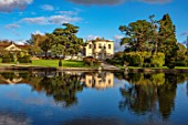 THORP PERROW ARBORETUM, YORKSHIRE: CLIPPED TOPIARY YEW, HOUSE ACROSS THE LAKE IN AUTUMN. TREES, LAKES, WATER, EVENING LIGHT, REFLECTIONS, REFLECTED