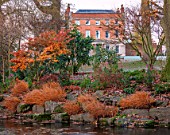 MORTON HALL GARDENS, WORCESTERSHIRE: THE HALL FROM THE STROLL GARDEN, WINTER. HAKONECHLOA MACRA, ACER, MAPLES, TREES, SHRUBS