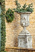 DAYLESFORD ORGANIC, GLOUCESTERSHIRE: CHRISTMAS: WHITE URN, CONTAINER WITH SPRUCE CHRISTMAS DECORATIONS AND NATURAL WREATH ON WALL, WINTER