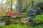 BATSFORD ARBORETUM, GLOUCESTERSHIRE: BRONZE CHINESE LION AND RED CHINESE WOODEN BRIDGE, SPRING, APRIL, CHINA