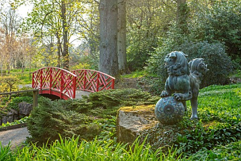 BATSFORD_ARBORETUM_GLOUCESTERSHIRE_BRONZE_CHINESE_LION_AND_RED_CHINESE_WOODEN_BRIDGE_SPRING_APRIL_CH