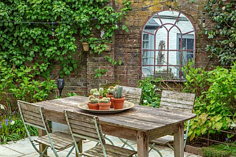 LITTLE_ORCHARDS_SURREY_DESIGNER_NIC_HOWARD_COURTYARD_PATIO_WOODEN_TABLE_CHAIRS_PAVING_MIRROR_SPRING_