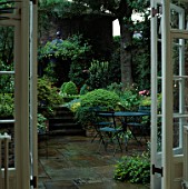 VIEW THROUGH FRENCH WINDOWS TO PAVED COURTYARD DINING AREA. STEPS FLANKED BY LUSH FOLIAGE. DESIGNER: JILL BILLINGTON