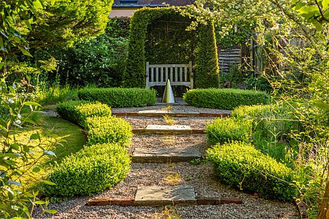 COTTAGE_ROW_DORSET_GRAVEL_PATH_TO_YEW_ARCH_WITH_WOODEN_SEAT_BENCH_BOX_HEDGING_WATER_FEATURE_GREEN_FO