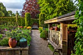 YORK GATE, YORKSHIRE: HERB GARDEN, JUNE, SUMMER, CLIPPED TOPIARY HEDGES, COLUMNS, WOODEN BENCH, SEAT, WOVEN WILLOW HOOD, POTTING SHED, PATH