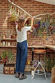 BEX PARTRIDGE, BOTANICAL TALES: BEX IN HER STUDIO TYING BUNCHES OF HARVESTED FLOWERS ON BRANCH TO NATURALLY AIR DRY. RIBBONS FROM NATURAL DYEWORKS