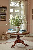 ASHBROOK HOUSE, NORTHAMPTONSHIRE: HALLWAY WITH WHITE COSMOS IN CONTAINER ON WOODEN TABLE WITH BOOKS