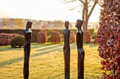 LOWER BOWDEN MANOR, BERKSHIRE: SPRING, APRIL, SUNRISE, MORNING, MAIN LAWN, BEECHHEDGES, HEDGING, CONES, SCULPTURES BY LAURENCE BONNEL