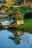 LOWER BOWDEN MANOR, BERKSHIRE: SPRING, APRIL, POND, POOL, CLOUD PRUNED TREE, WOODEN BOX, CONTAINER, REFLECTIONS, REFLECTED
